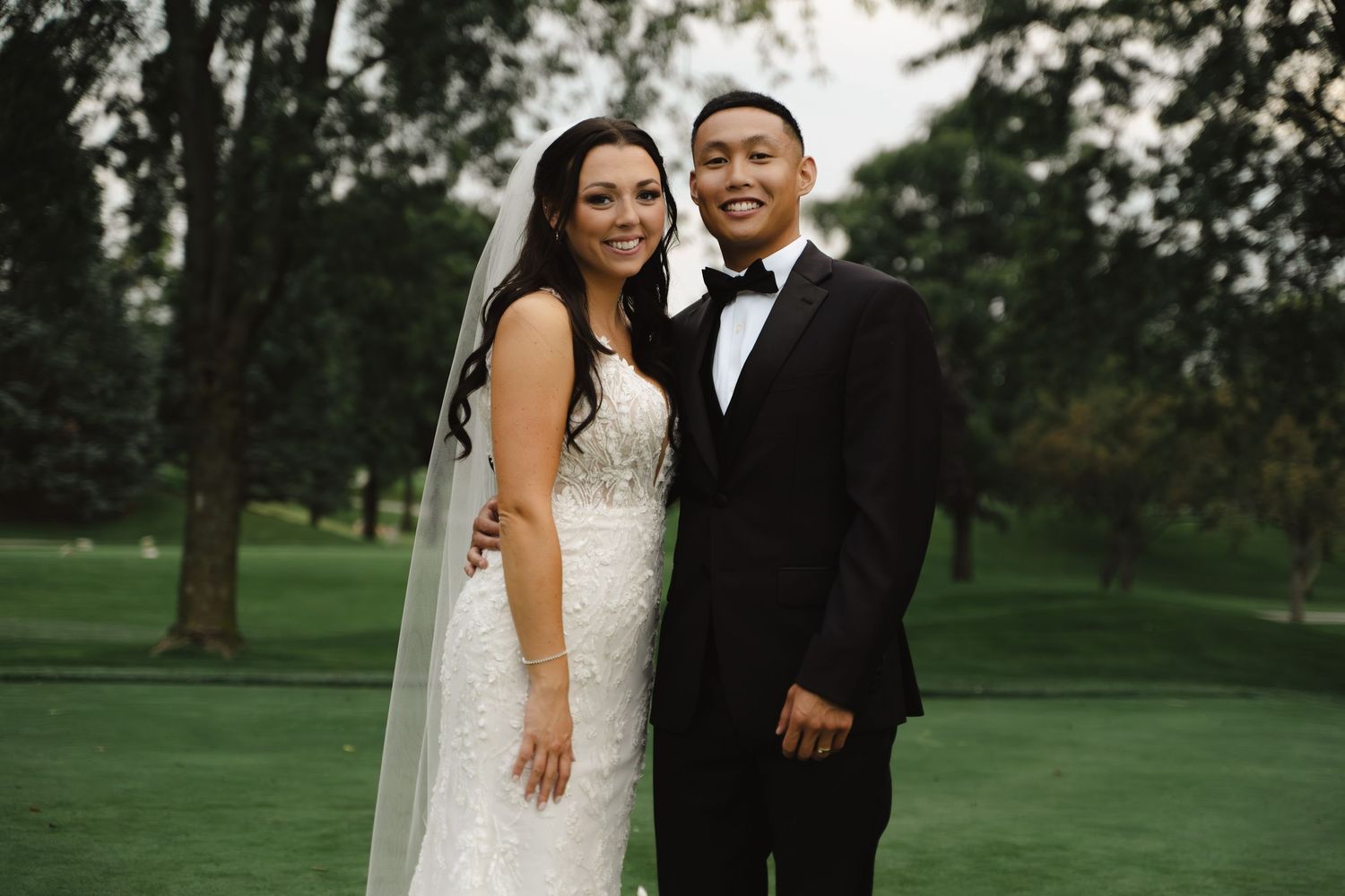 Bride and groom smile together on golf course in wedding attire on their special day.