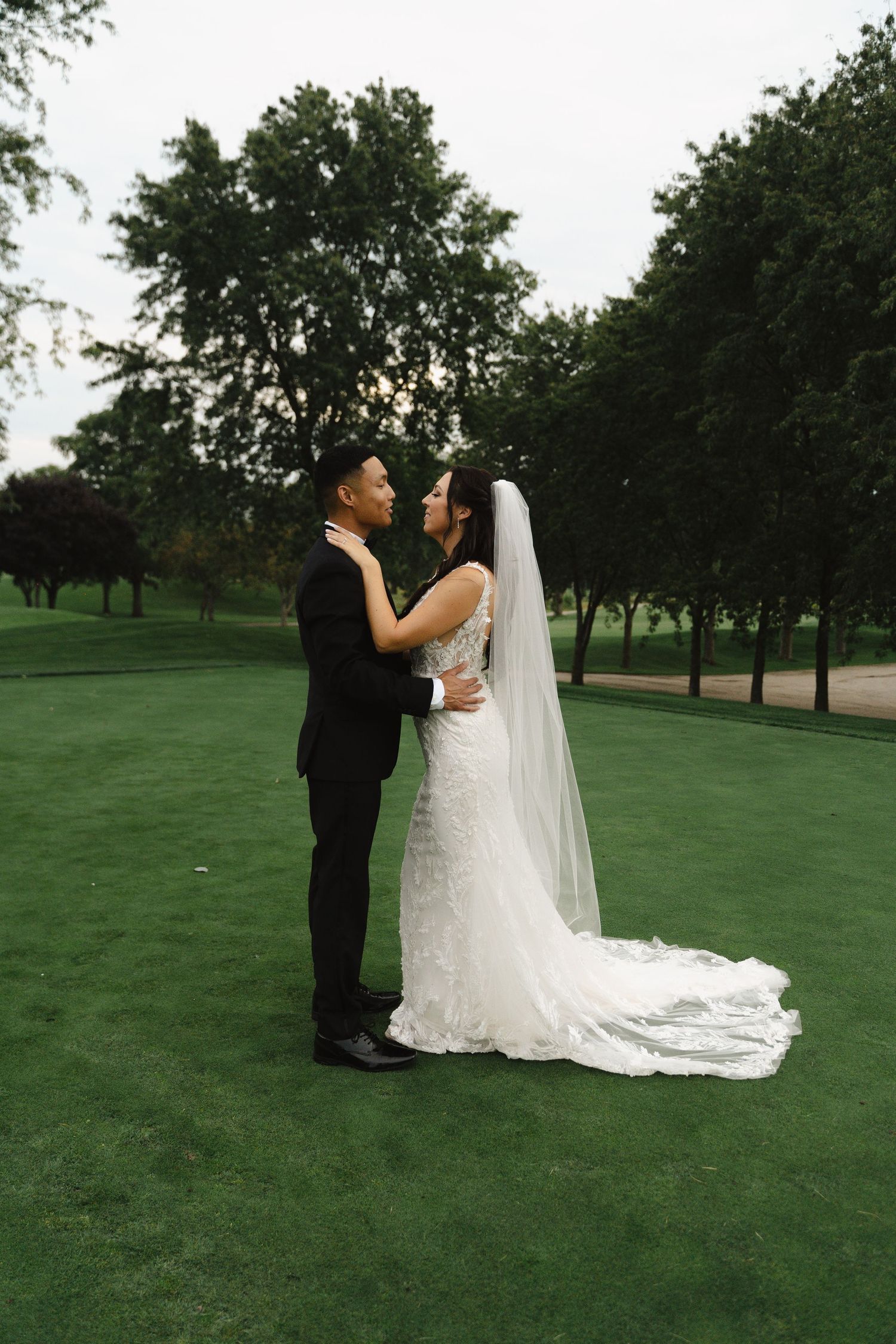 Bride and groom share romantic moment on lush green golf course at dusk.