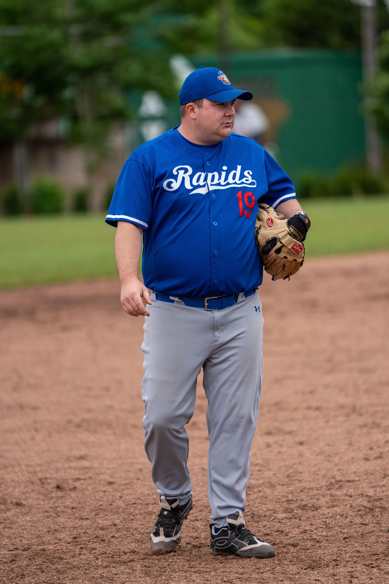 Baseball player in blue Rapids jersey number 19 holds glove on dirt infield during game.