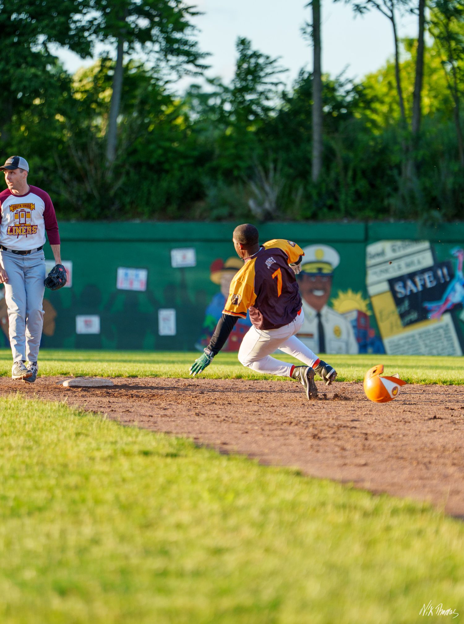 Baseball player number 7 slides into base during a game while opponent watches.