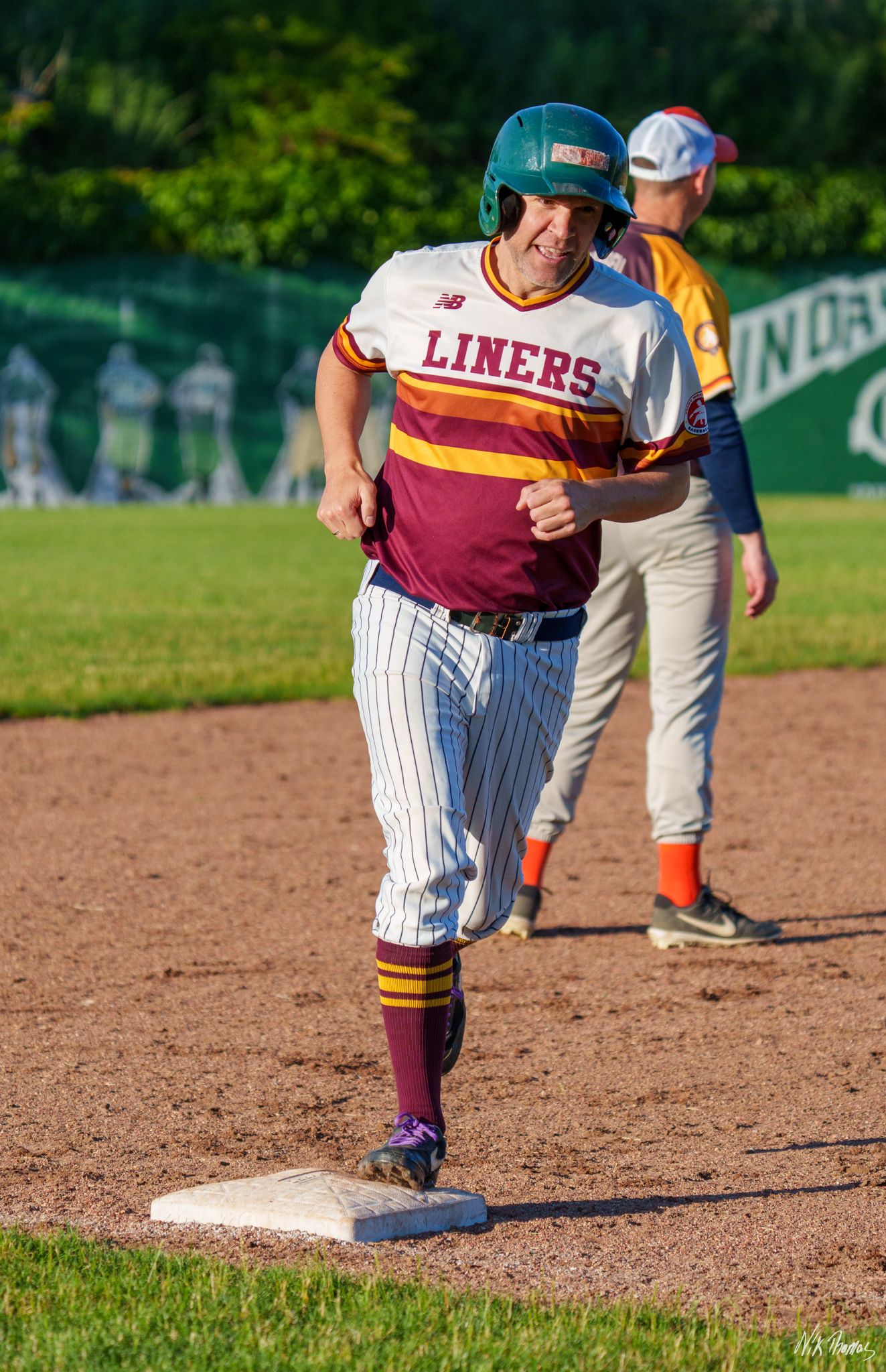 Smiling Liners baseball player steps on base wearing a teal helmet.