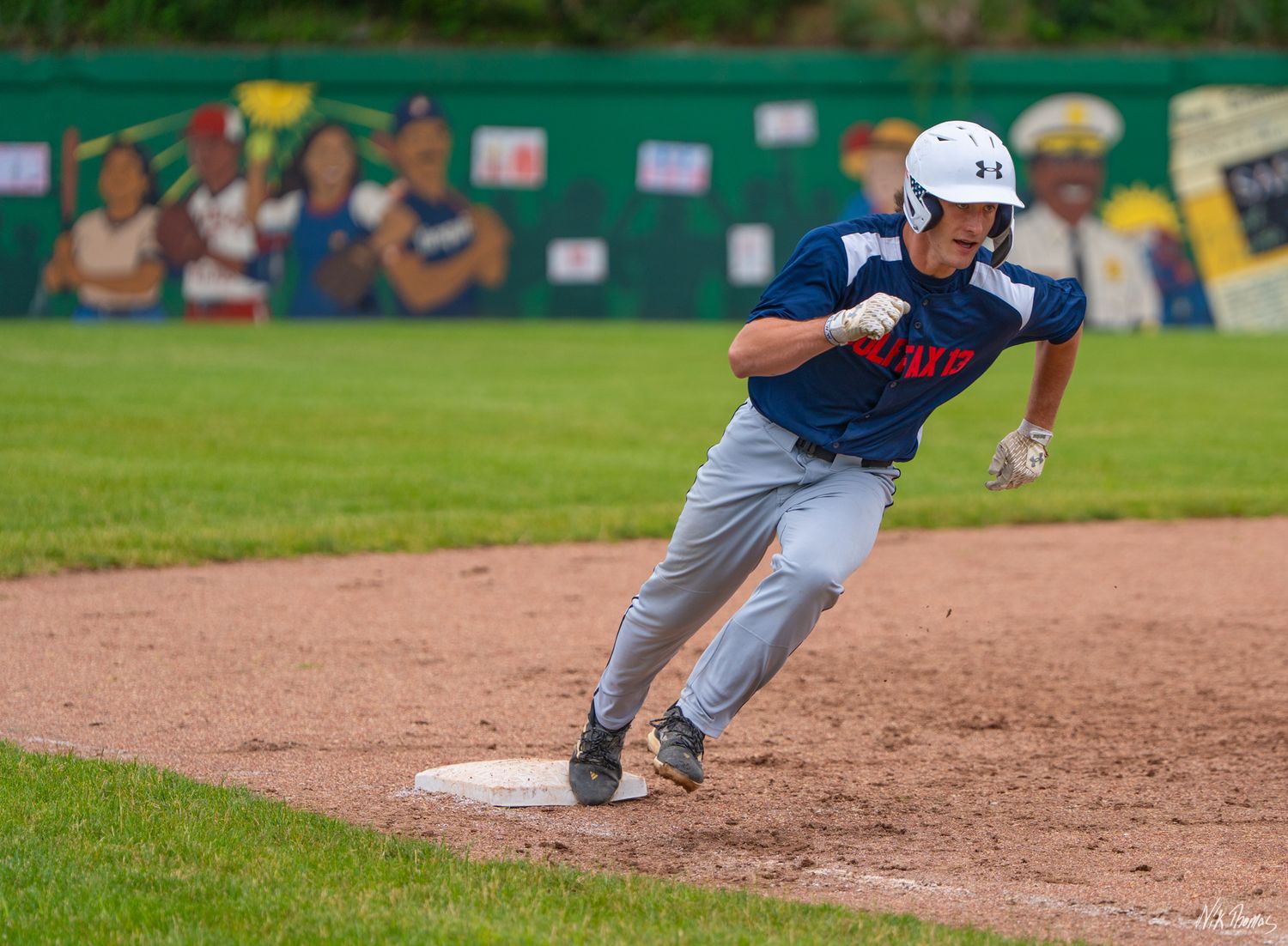 Baseball player rounds third base at full speed during an outdoor game.
