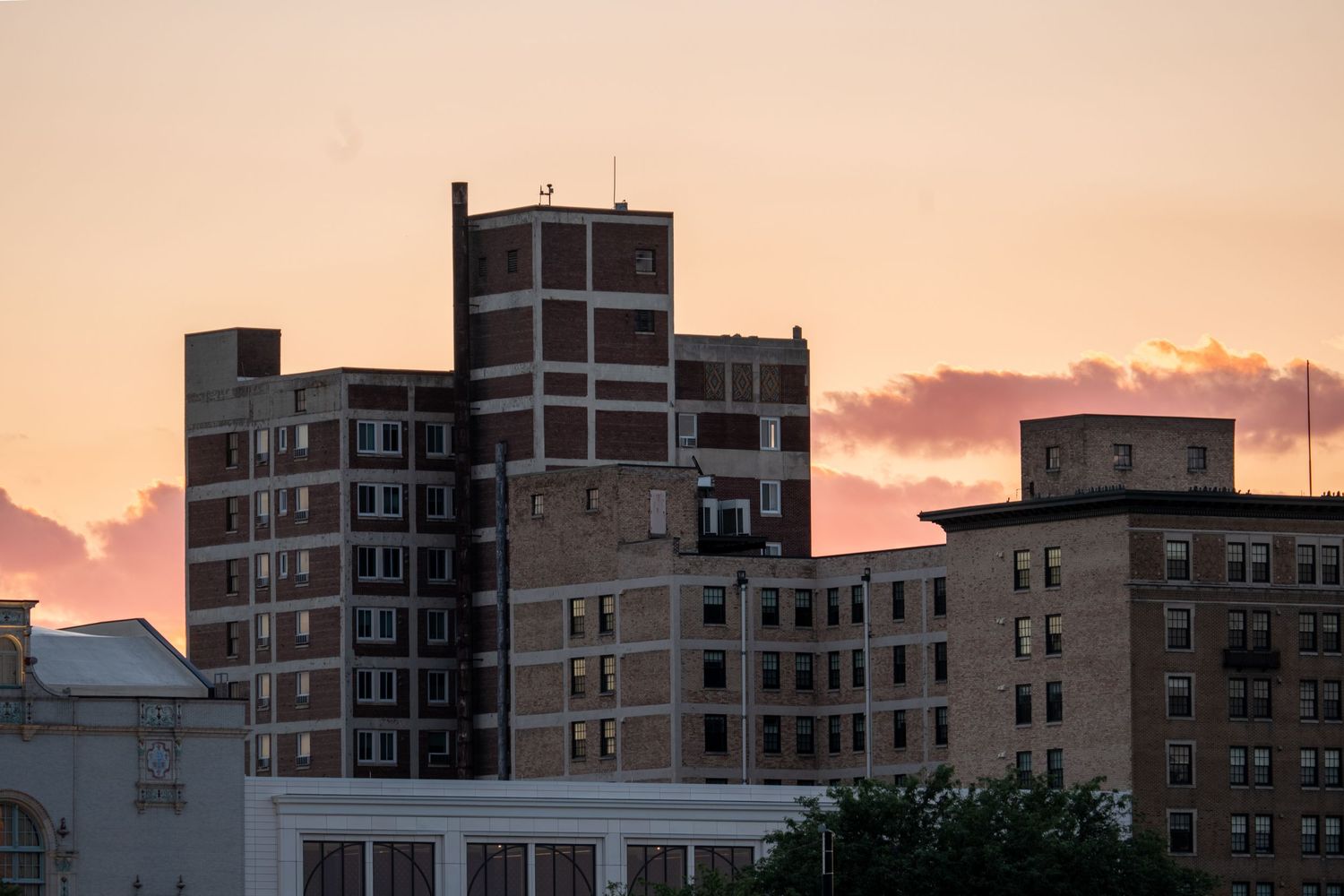 Historic brick buildings silhouetted against a vibrant orange and pink sunset sky in urban downtown.
