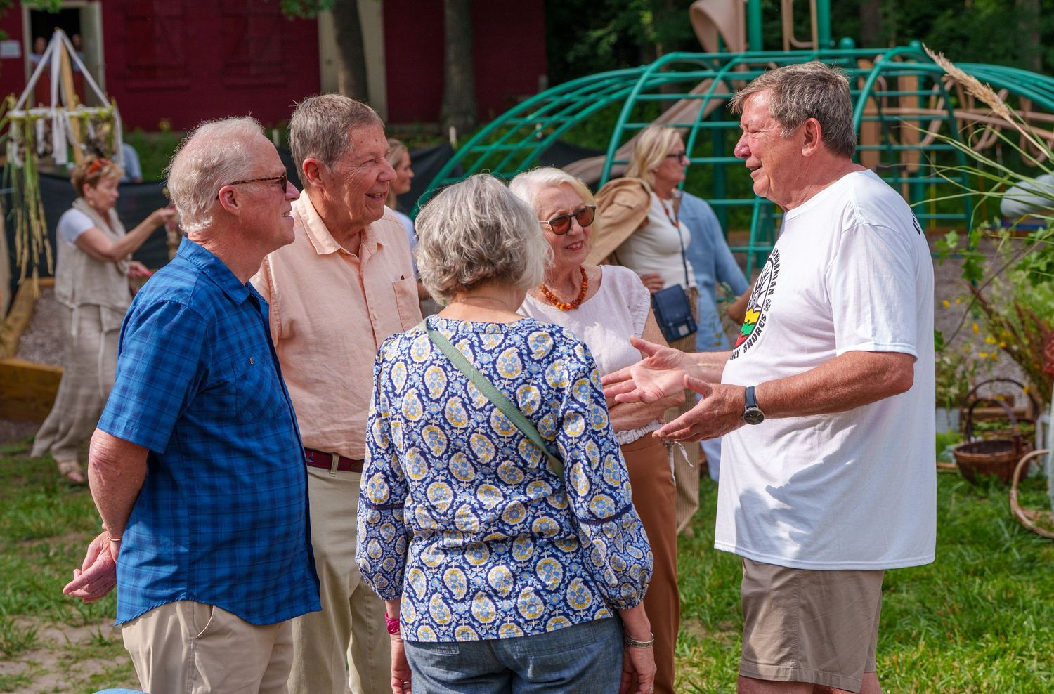 Group of seniors socializing outdoors at a summer garden event near a red barn.