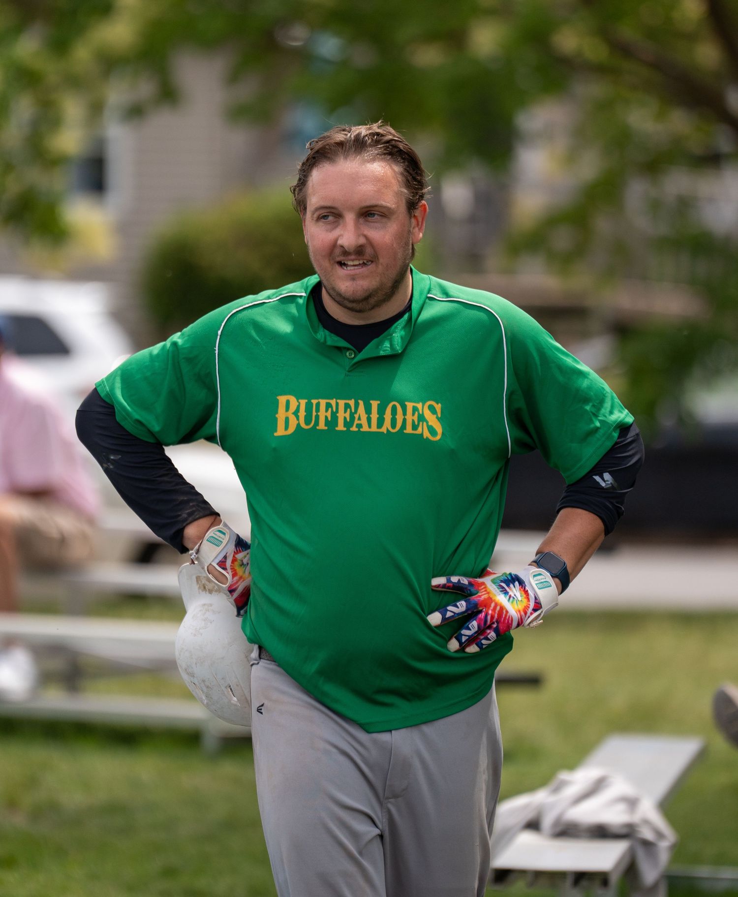 Smiling baseball player in green Buffaloes jersey with batting gloves stands on field with hands on hips.