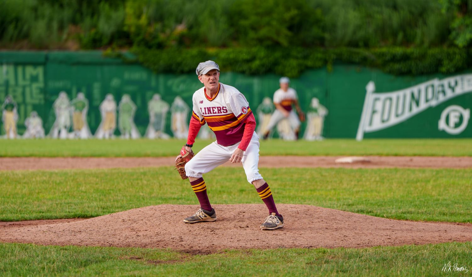 Baseball pitcher in red and white uniform ready on the mound at Foundry Field during a sunny game.