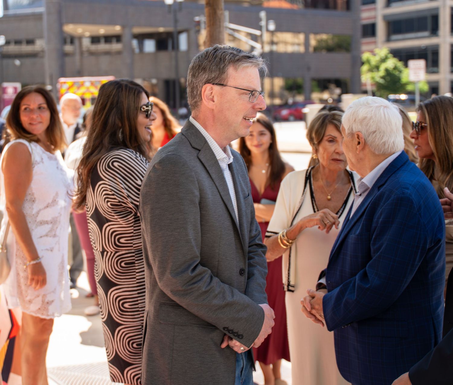 Professionals networking outdoors at a business event in an urban setting on a sunny day.