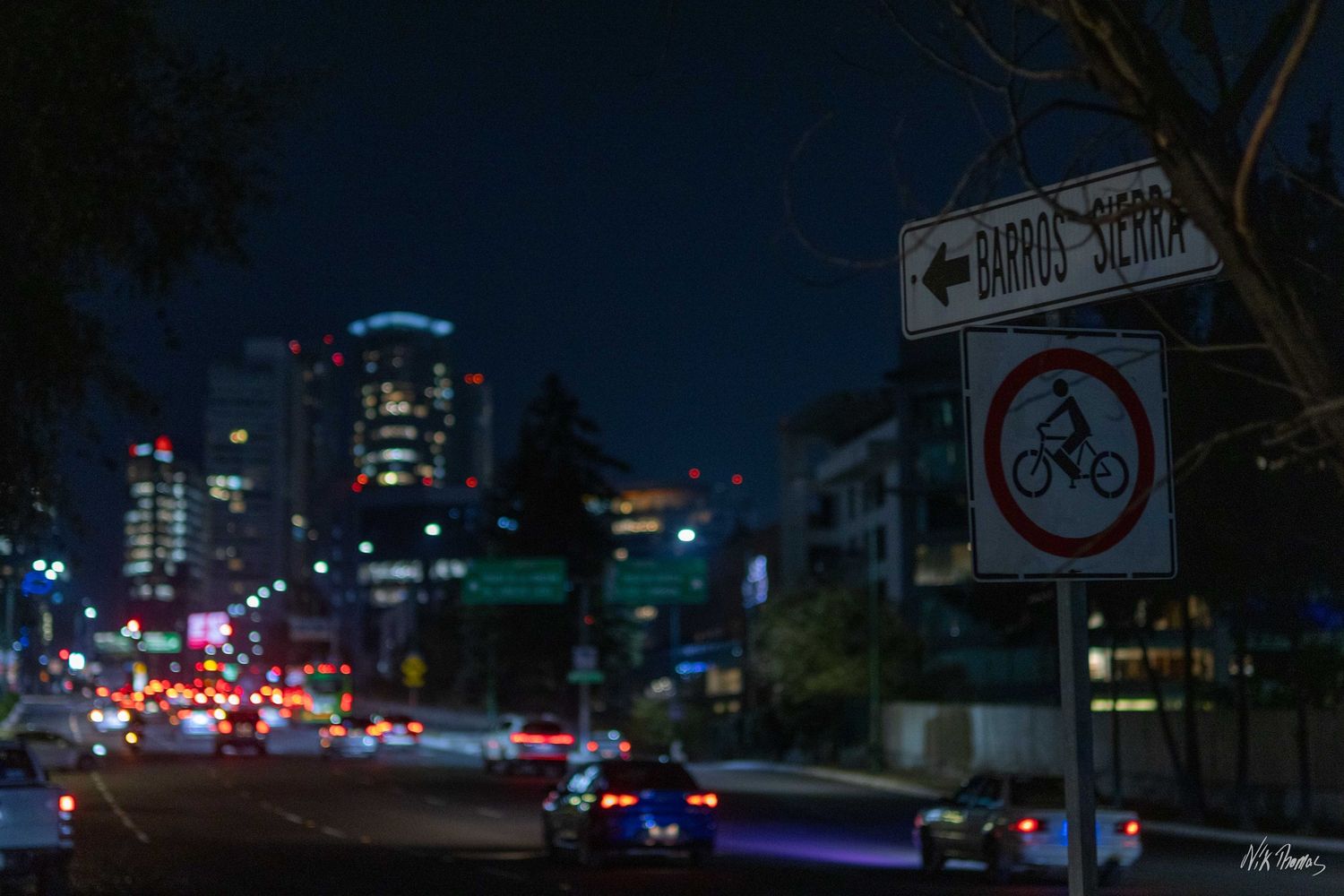 Night cityscape with illuminated street signs for Barros Sierra and a no-cycling symbol in Mexico City.
