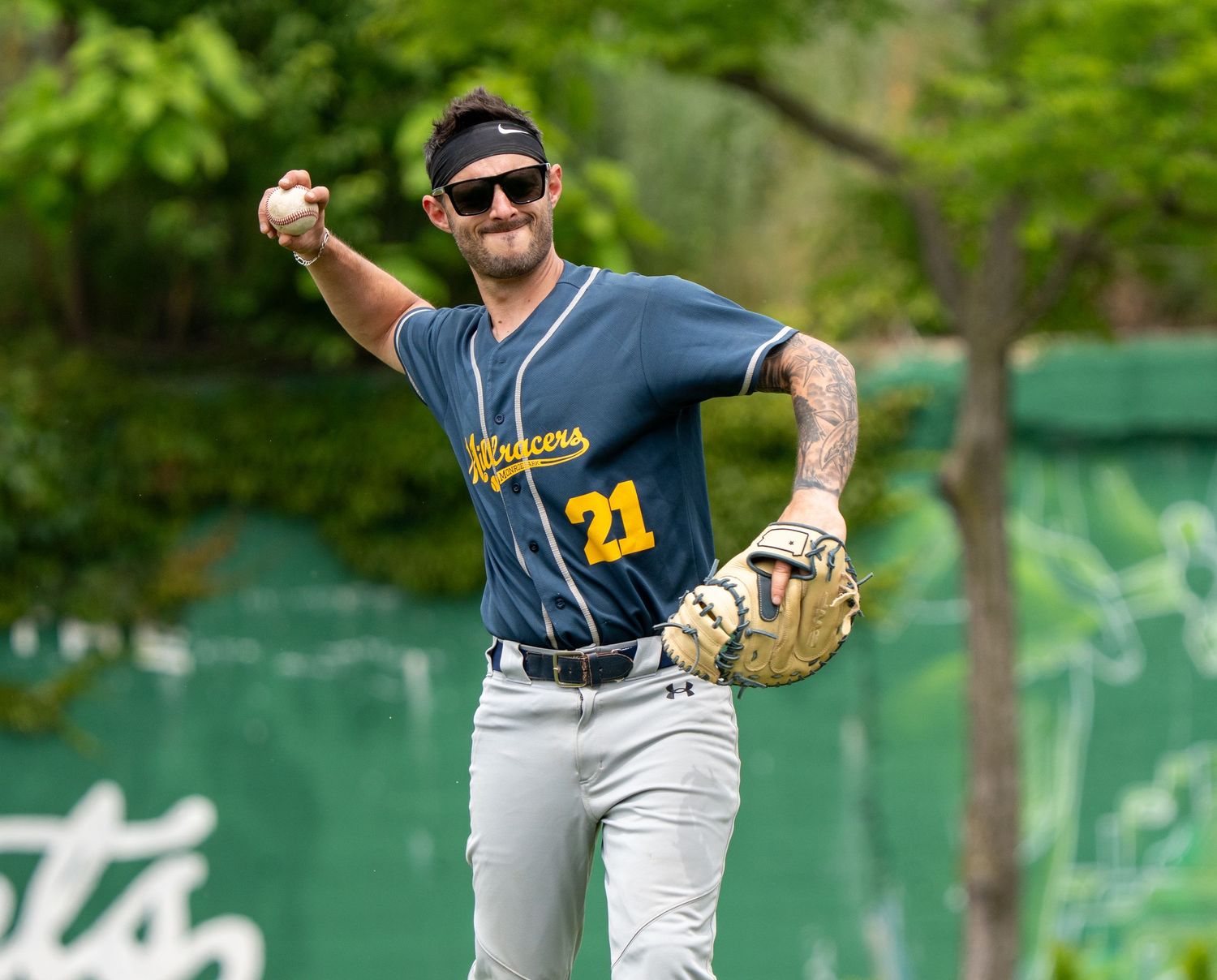 Baseball player #21 in navy jersey throwing ball on field, wearing sunglasses and batting glove.