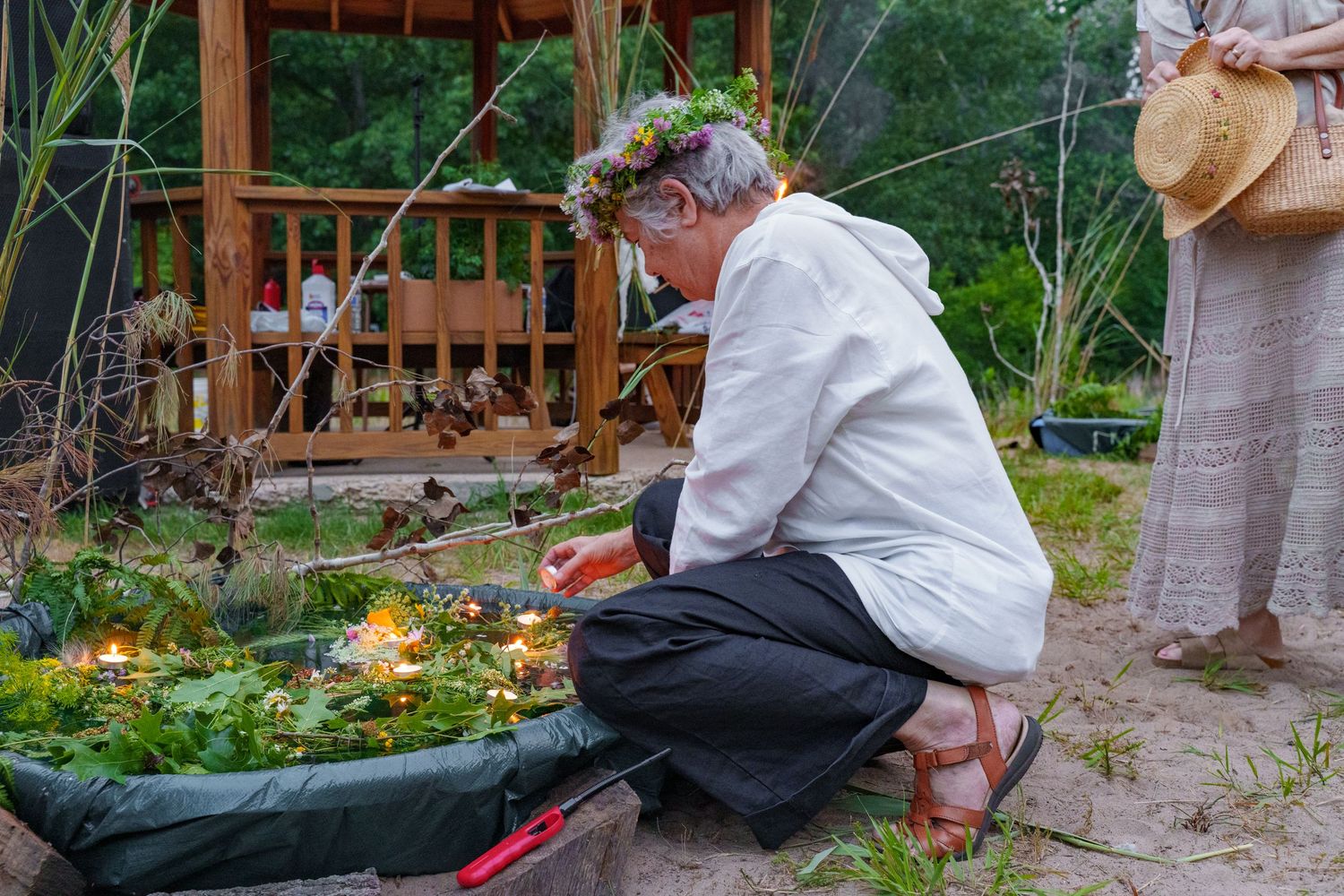 Elderly person placing floral offerings near candles during a traditional midsummer ritual ceremony.