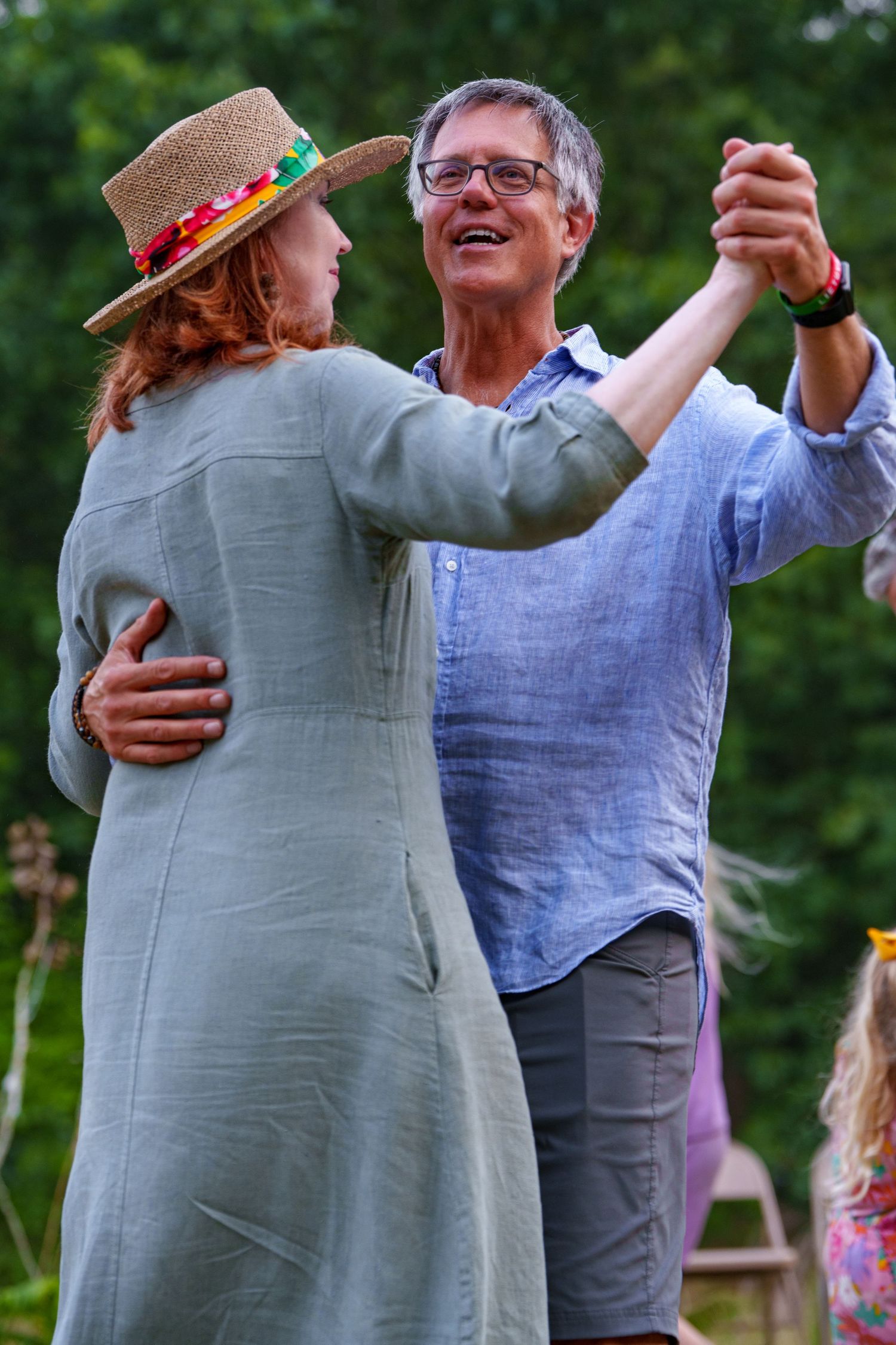 Smiling couple dancing outdoors at a summer folk festival surrounded by greenery.