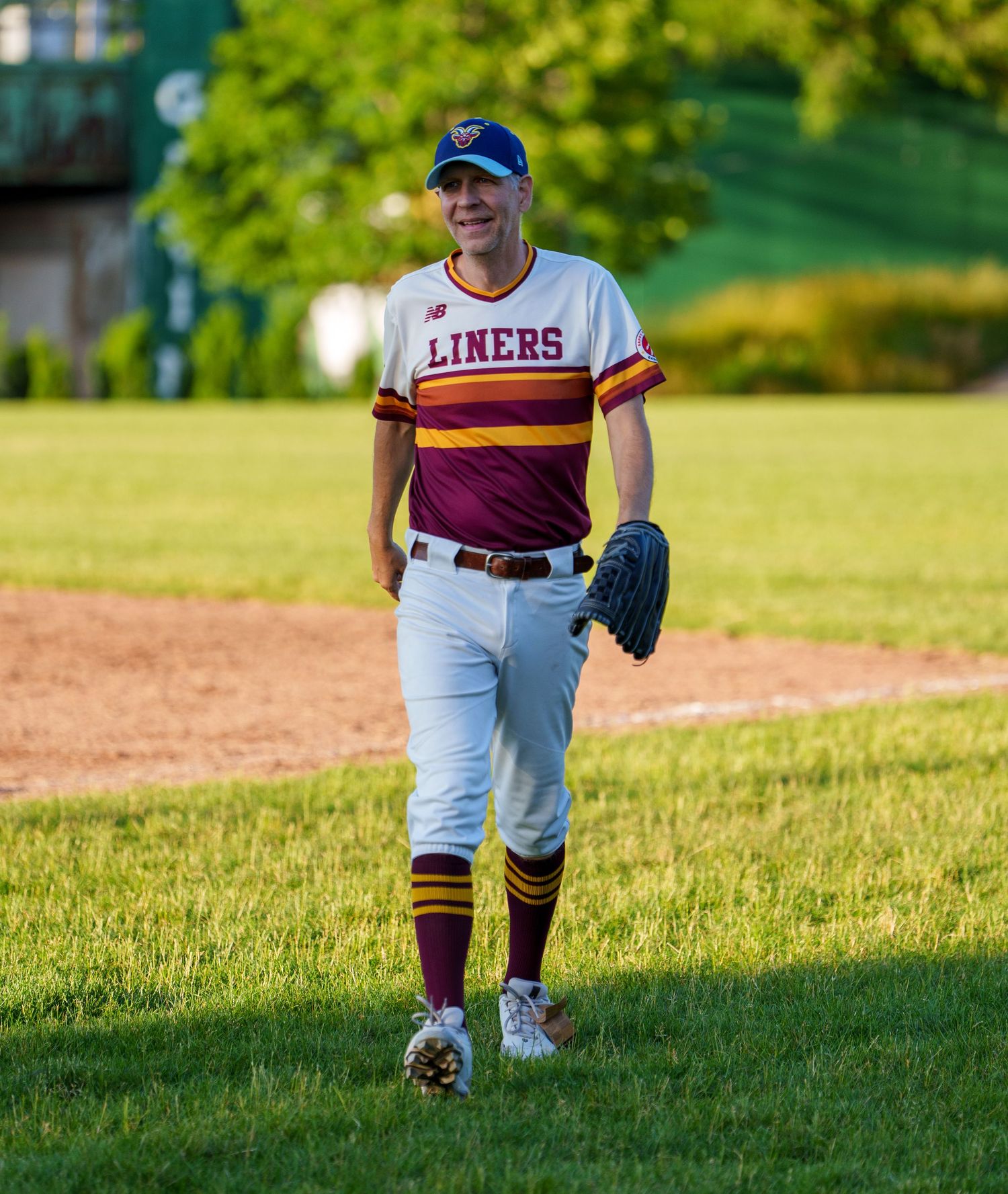Baseball player in Liners uniform walking on field with glove, wearing maroon and white jersey and cap.
