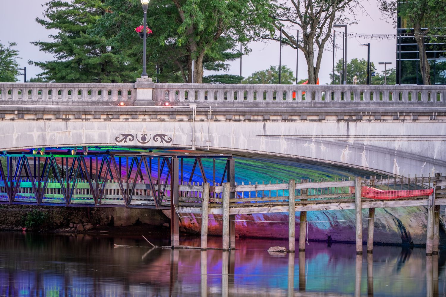 Colorful graffiti art decorates the underside of a white stone bridge reflected in calm river water.