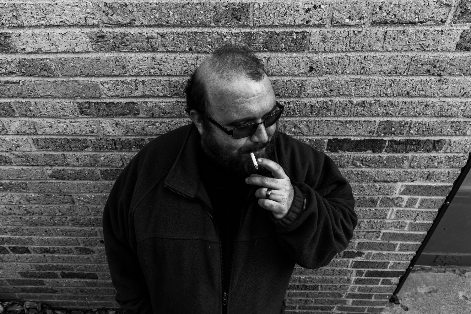 man smoking a cigarette while leaning against a brick wall