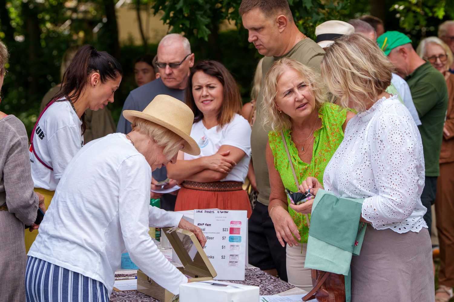 Group of people gathered around a table reviewing materials at an outdoor summer event.