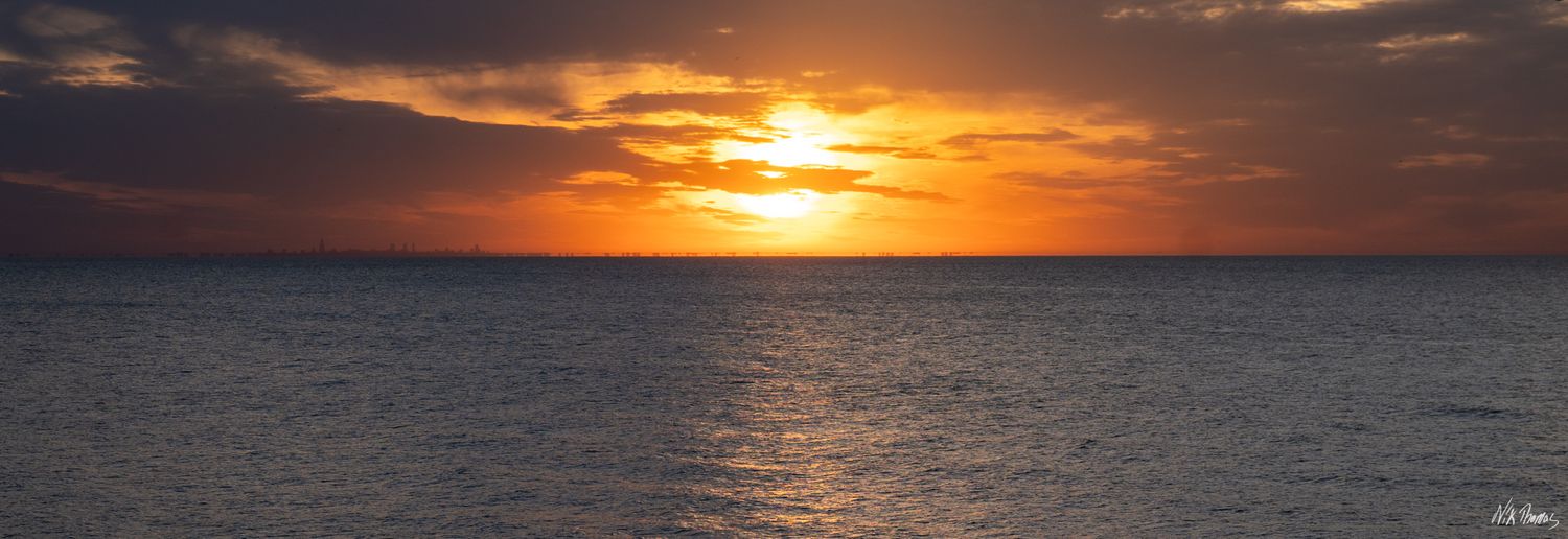 Stunning panoramic ocean sunset with vibrant orange and red sky reflecting on calm sea waters.