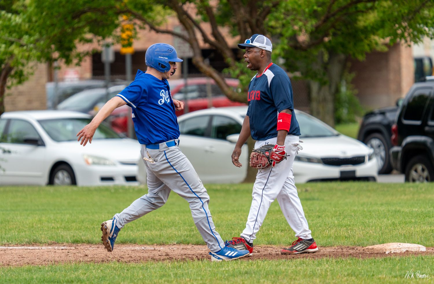 Baseball player in blue uniform running bases as a fielder in navy uniform stands near first base.
