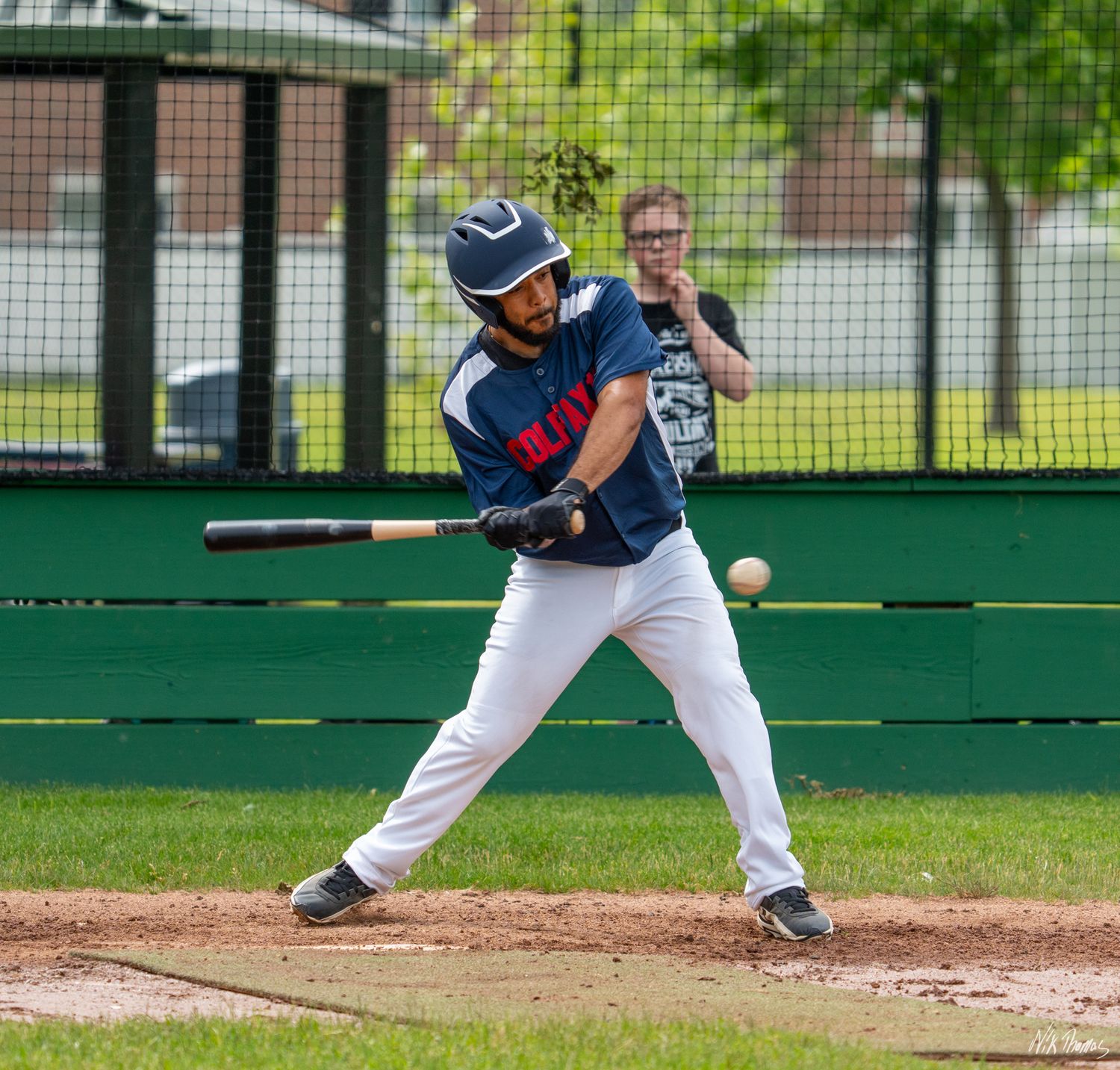 Baseball batter swinging at a pitch during an outdoor game, wearing a navy blue uniform and helmet.