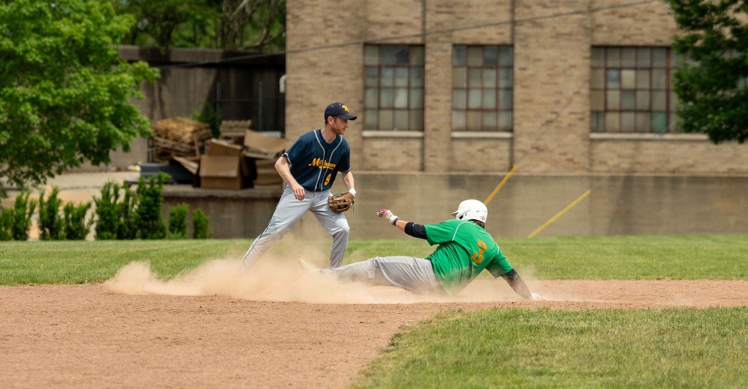 Baseball player slides into base creating dust cloud as fielder attempts tag during youth league game.