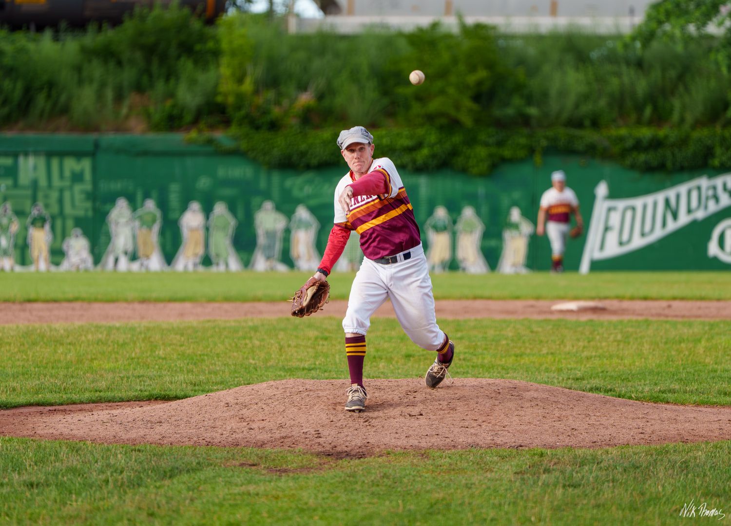 Baseball pitcher in white and red uniform mid-throw on mound during sunny game.