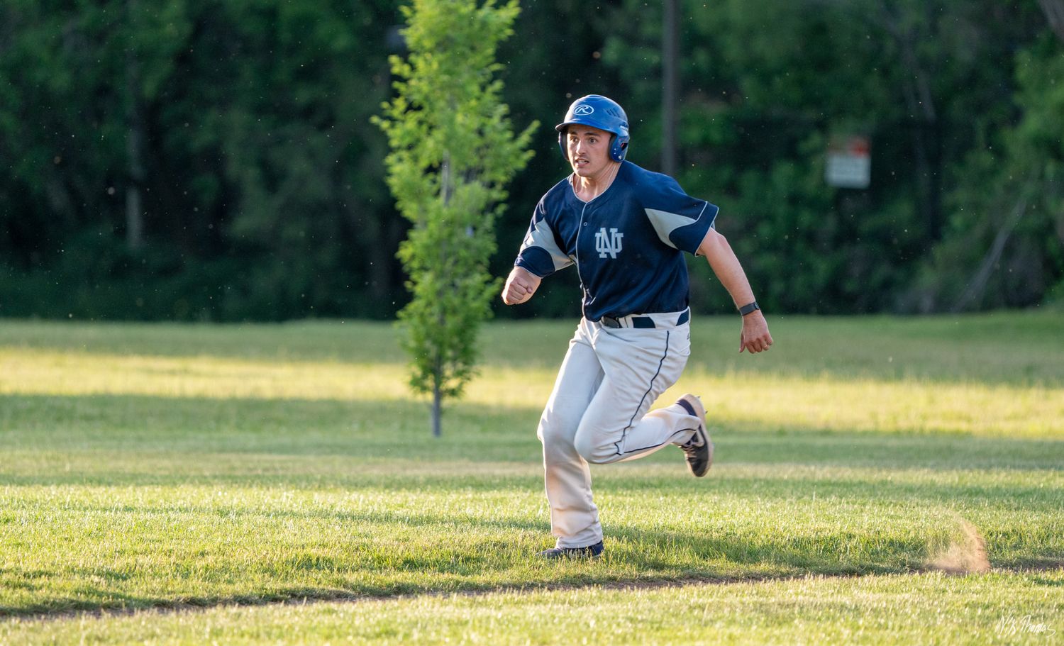 Baseball player in blue helmet sprinting across green grass field during a sunny outdoor game.