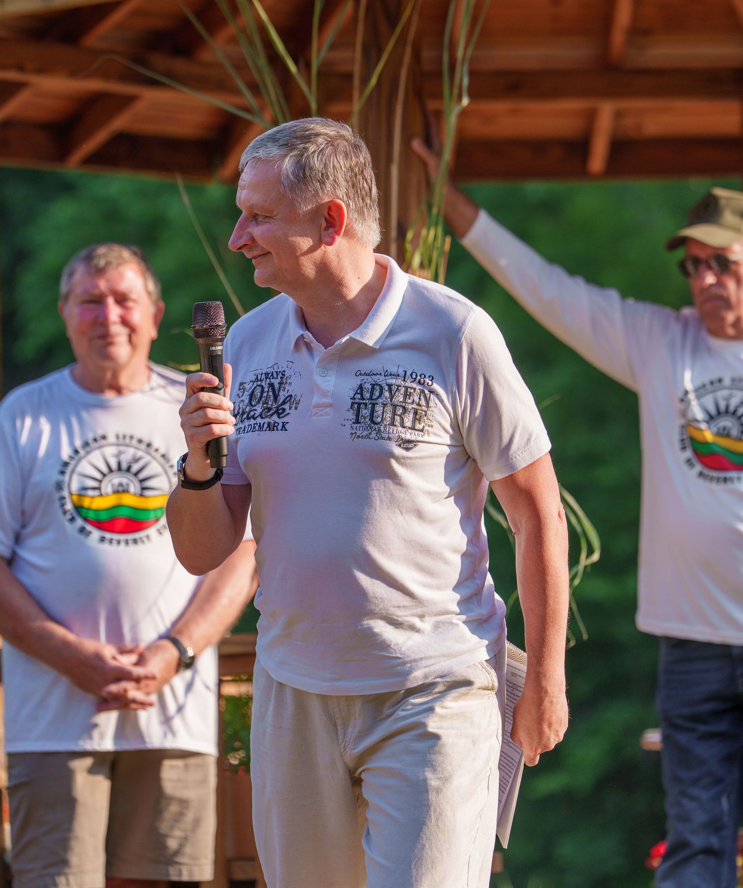 Man speaking into microphone at outdoor Lithuanian cultural festival event in summer.