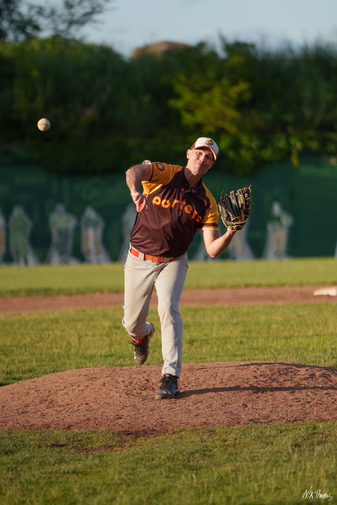 Liners pitcher releases ball from mound during evening baseball game.