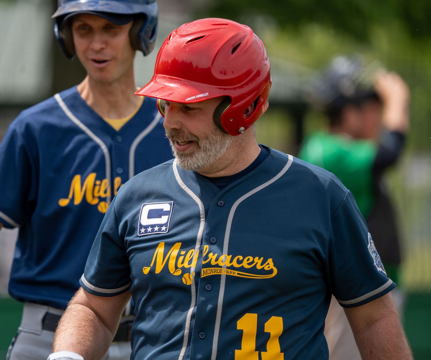 Two baseball players in Midtracers uniforms, one wearing red helmet, stand on field during game.