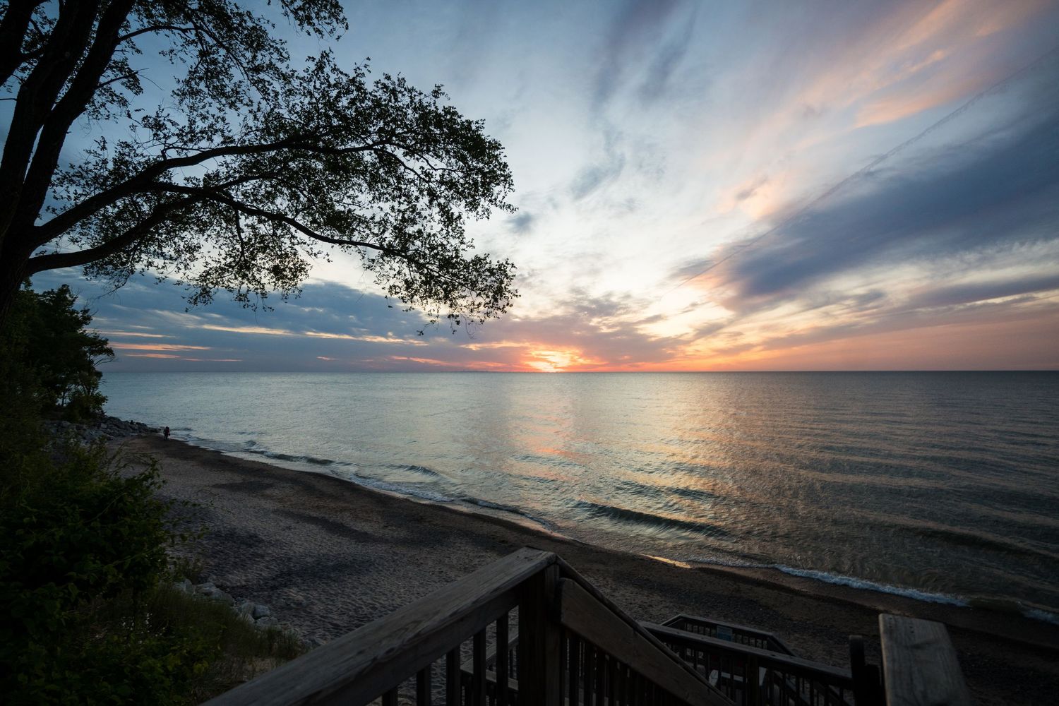 Stunning sunset over a calm lake with vibrant pink and blue sky, sandy beach, and a tree silhouette framing the scene.