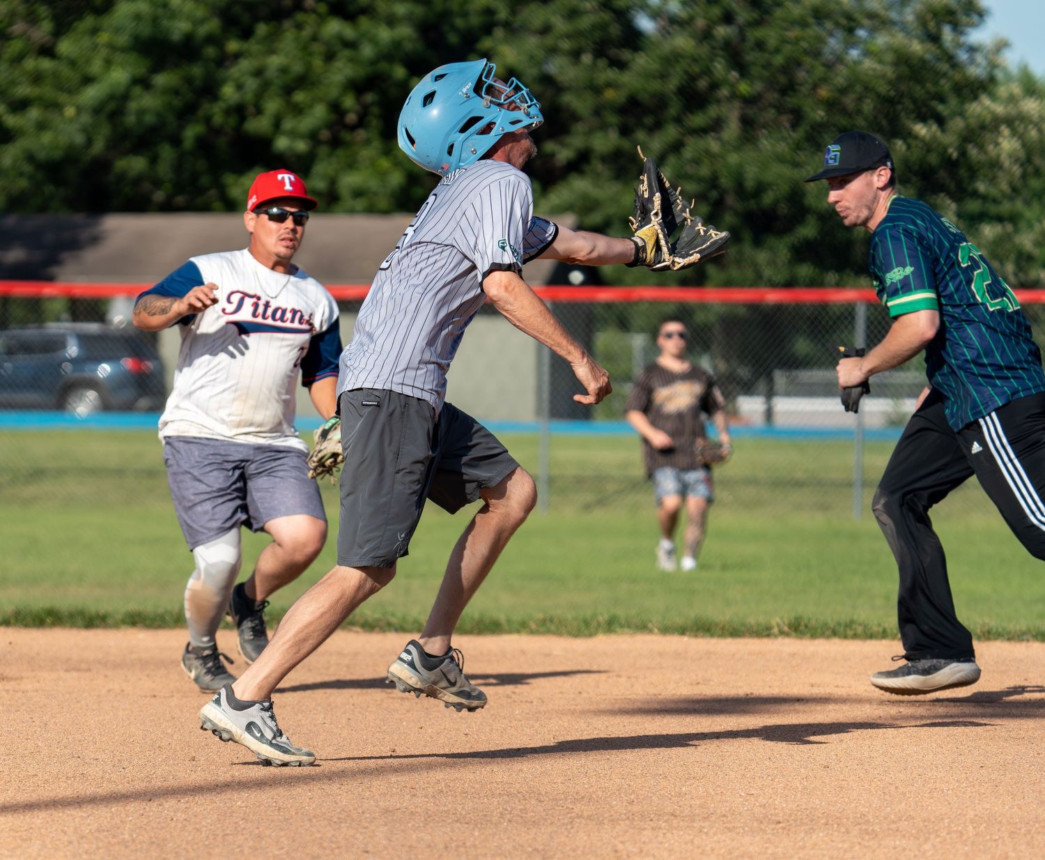 Players compete in a recreational baseball game on a sunny day, with a fielder catching the ball near base.