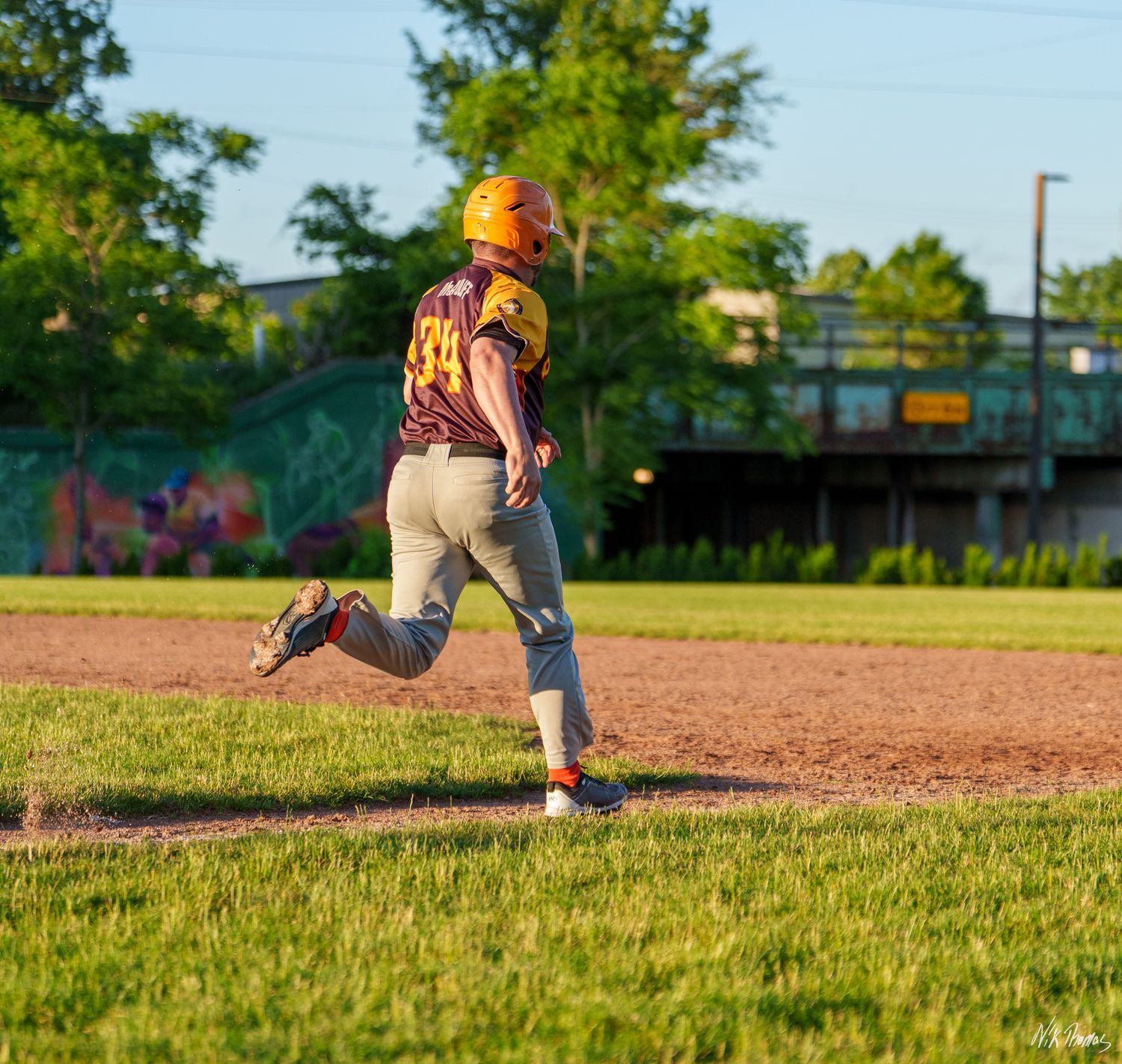 A baseball player in maroon and gold uniform rounds a base while running during an evening game.