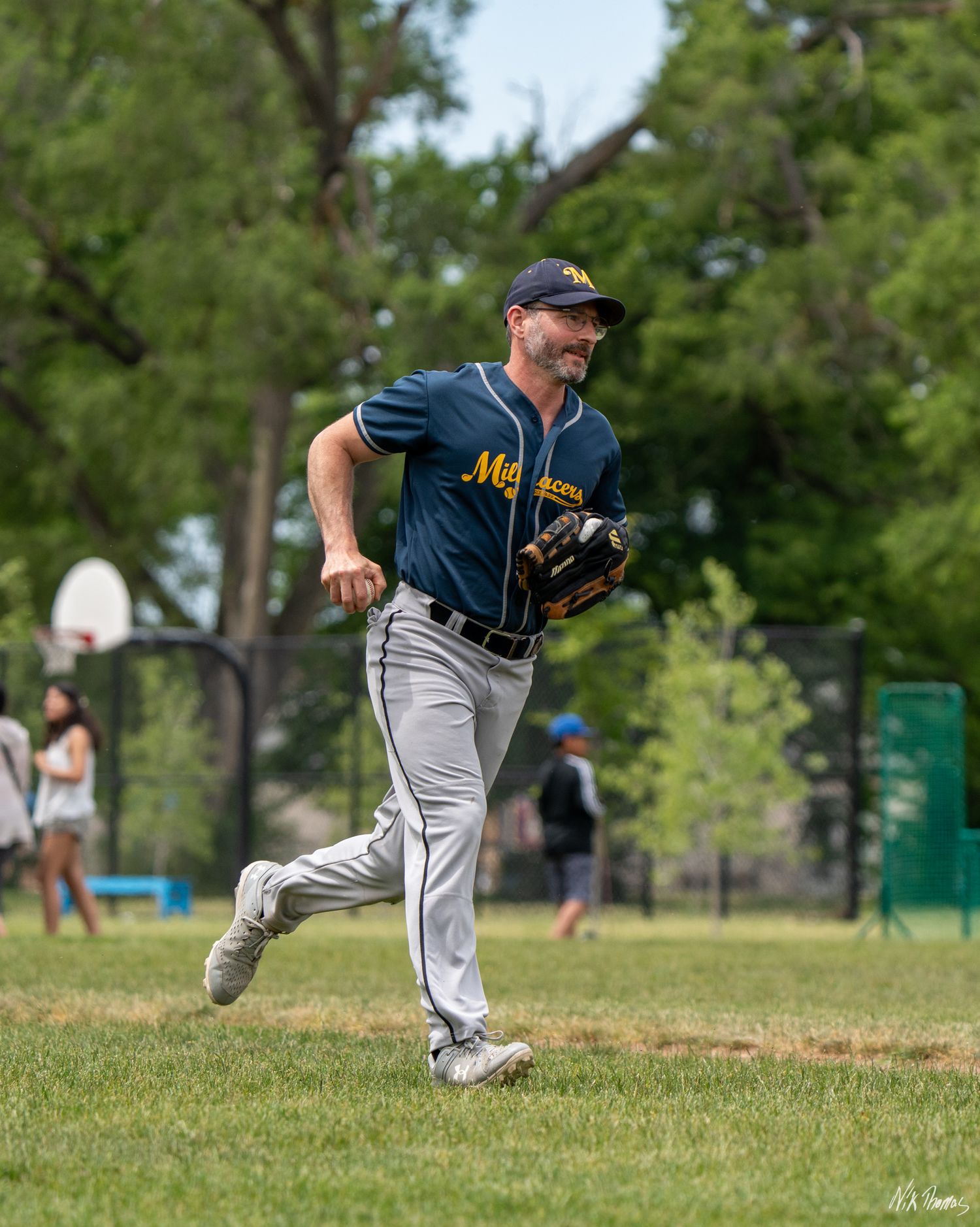 Smiling baseball player in navy Millers uniform runs across green field while holding glove.