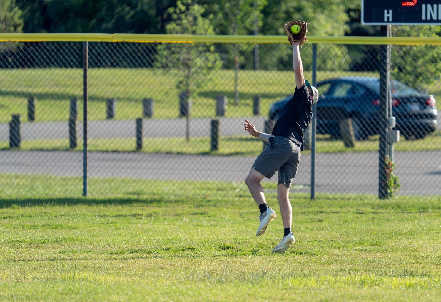 Player leaping to catch a softball in an outfield during a recreational game on a sunny day.