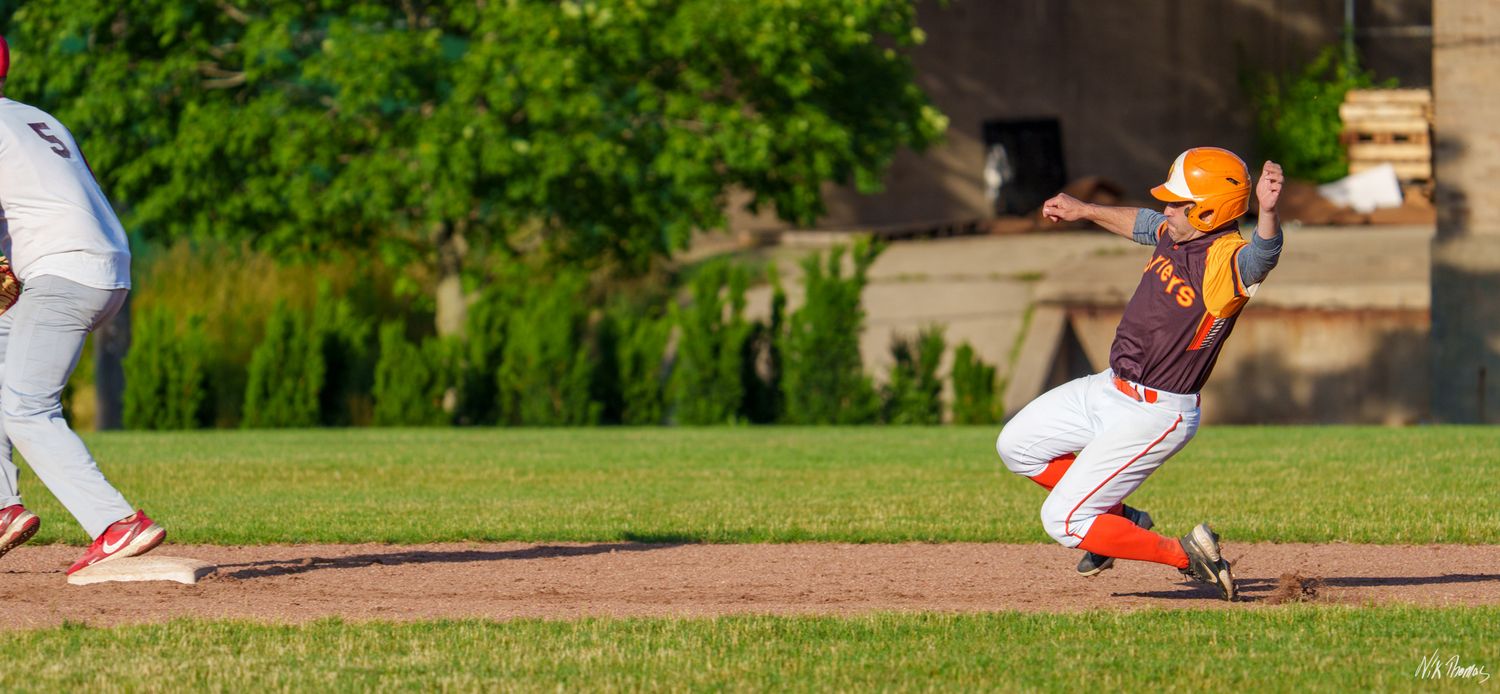 Baseball player in orange uniform sliding into base during a competitive outdoor game on a sunny day.