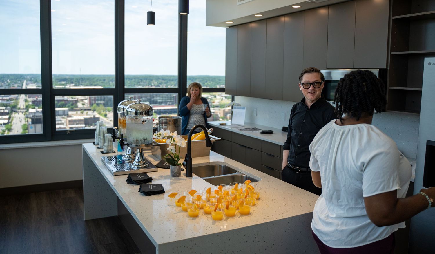 People gathered in modern high-rise kitchen with yellow rubber ducks on counter and city views.