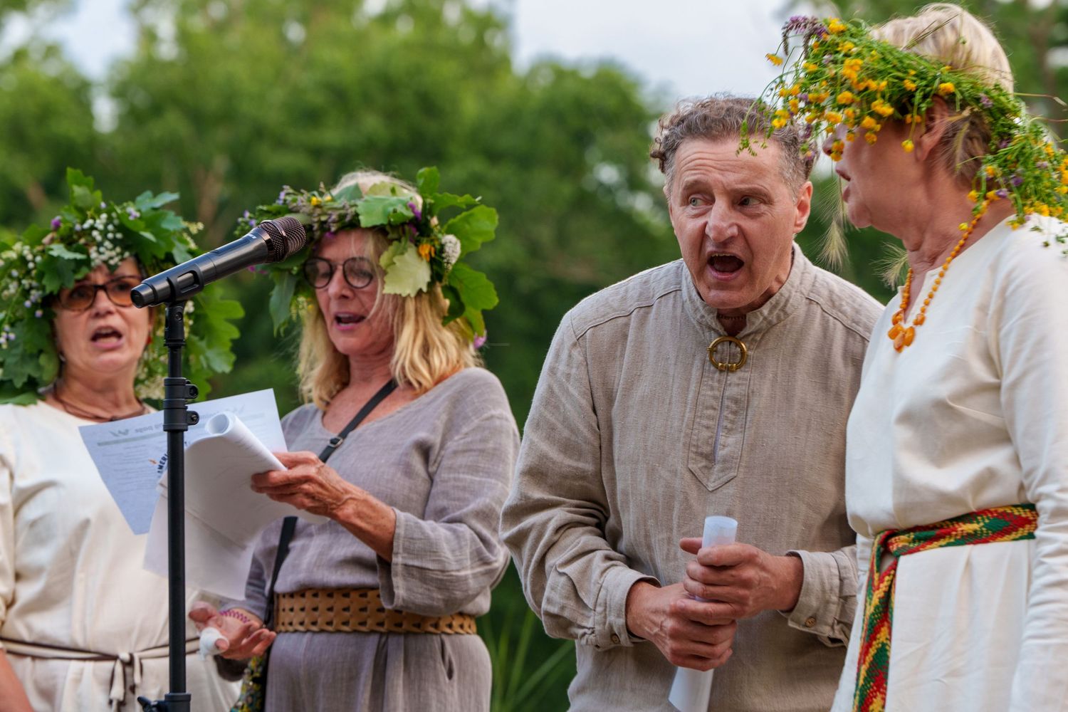 Group of four people singing outdoors wearing flower crowns and traditional folk costumes.