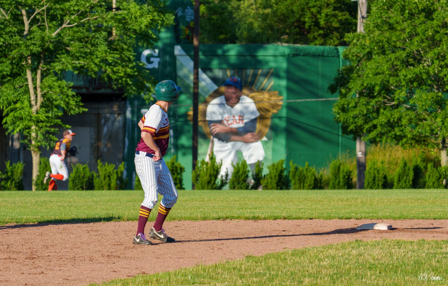 Baseball infielder in red and white uniform fielding near base on sunny day.