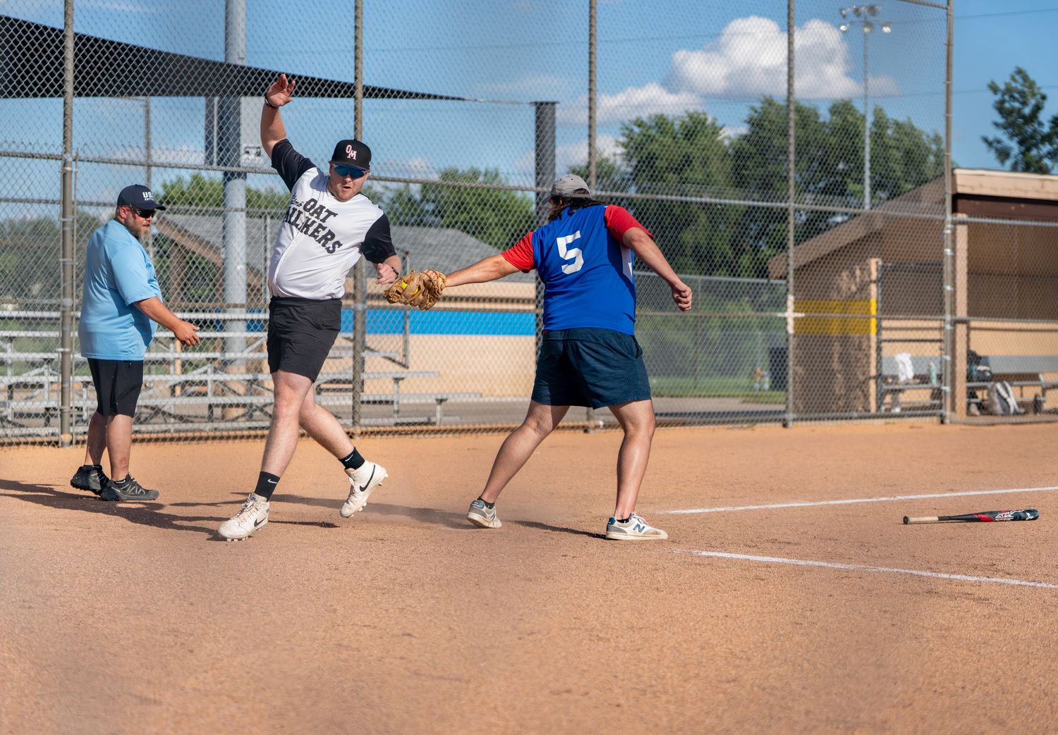Players compete in a recreational softball game on a sunny day, with a runner approaching base and fielder ready.