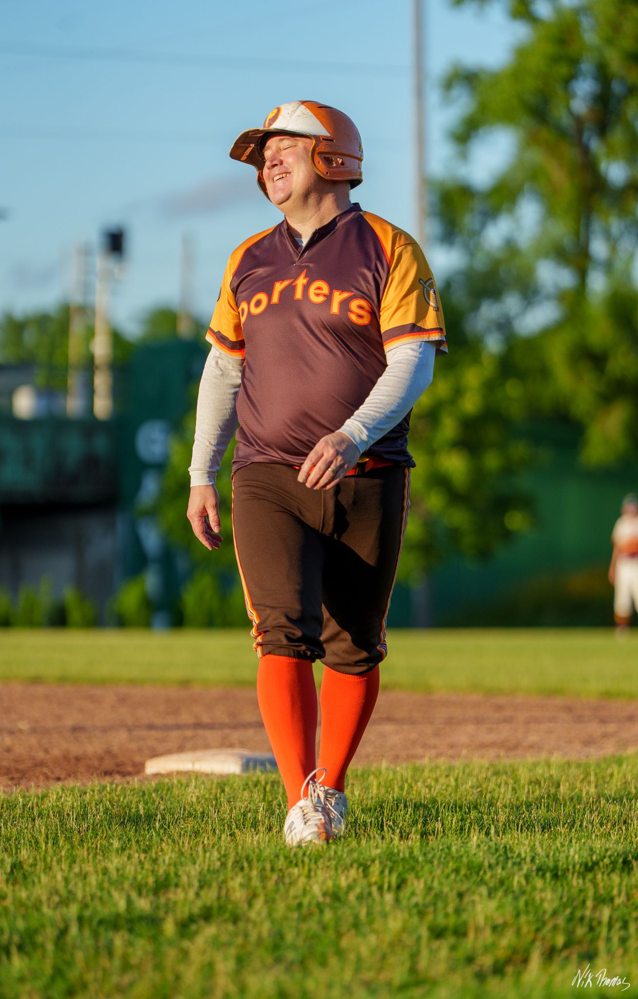Softball player in Porters uniform and orange socks smiling while standing on base during a game.