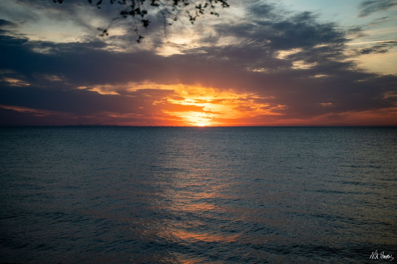 A stunning ocean sunset with vibrant orange and red hues reflecting on calm water under dramatic clouds.