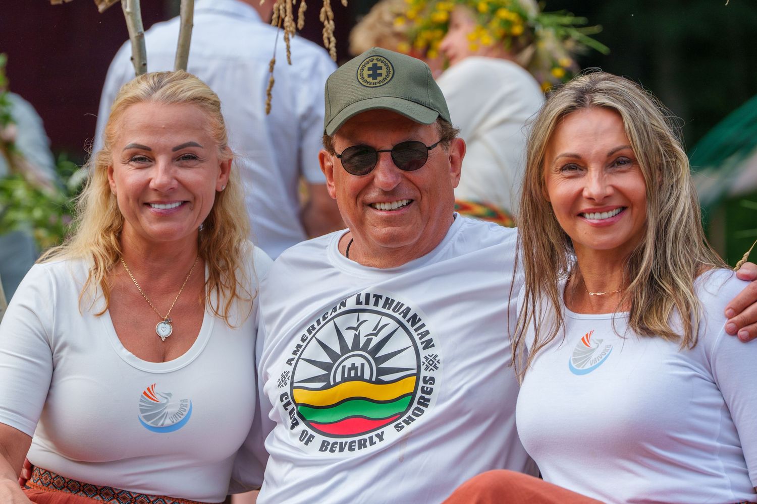 Three smiling adults pose together outdoors at a Lithuanian community event in Beverly Hills.