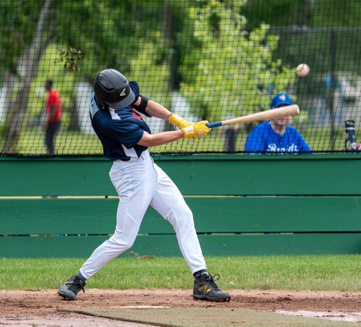 Young baseball batter in navy uniform makes contact with the ball during a game.