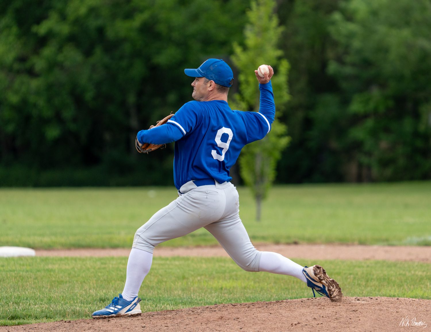 Baseball pitcher in blue jersey number 9 winds up to throw during an outdoor game.