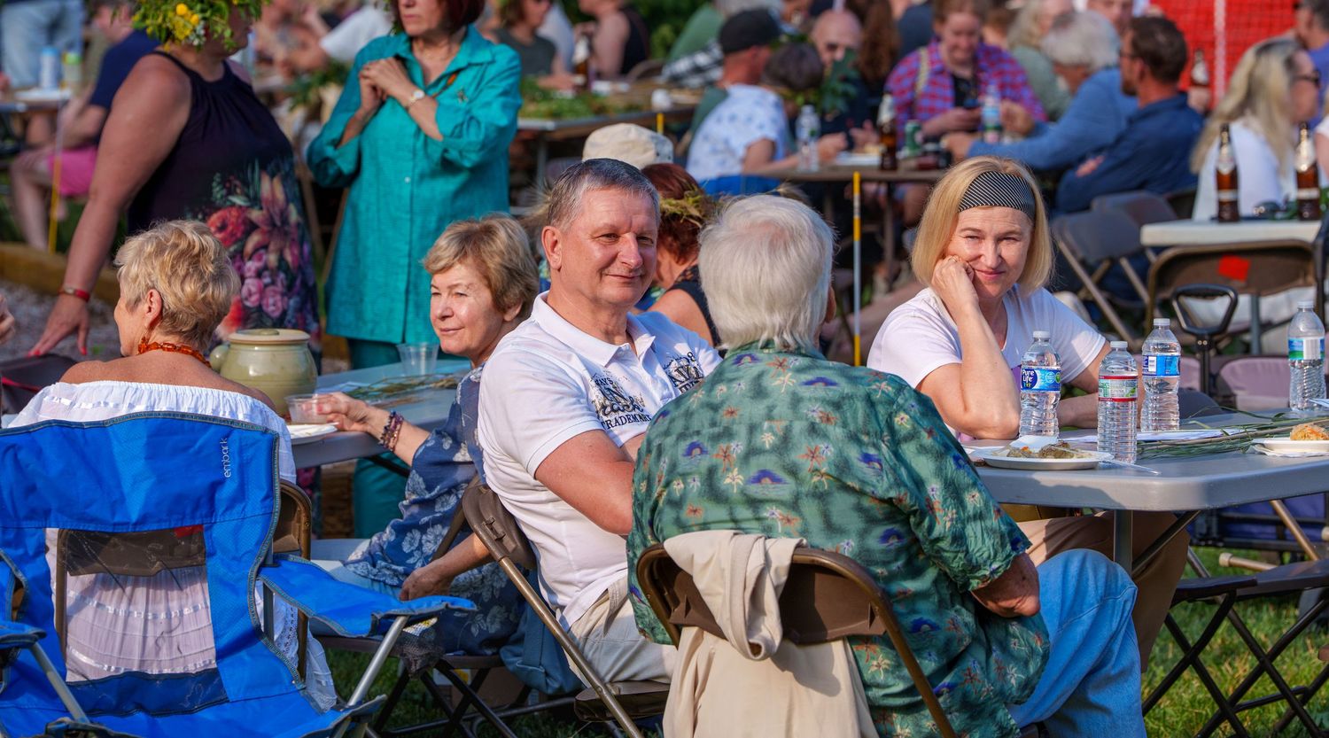 People socializing and smiling at outdoor community festival gathering at sunset.