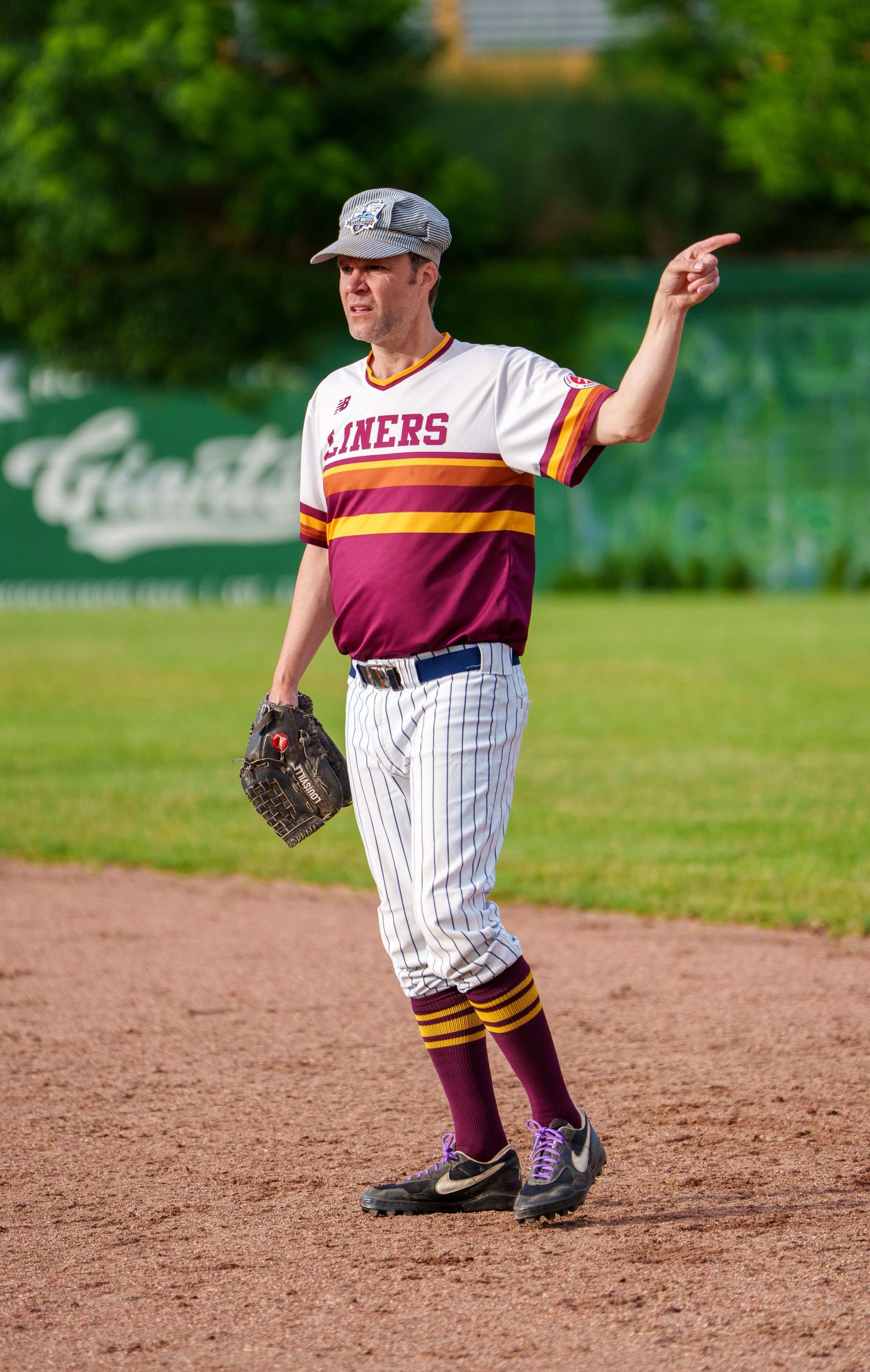 Baseball player in Liners uniform pointing while holding a glove on a dirt field.