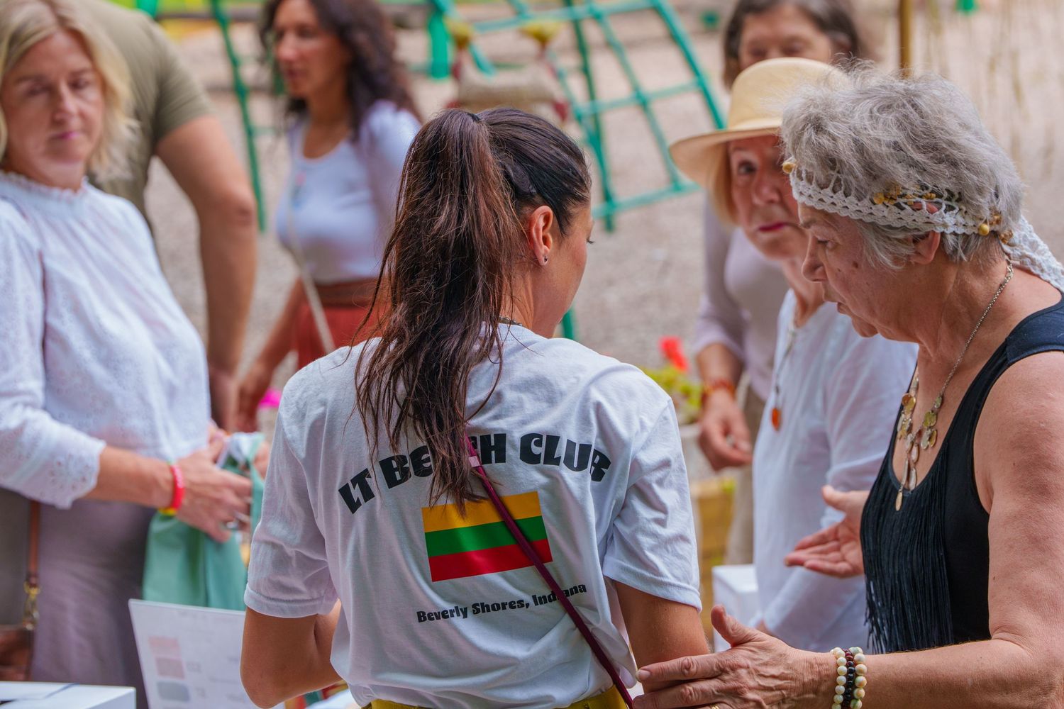 Woman in LT Beach Club shirt talks with silver-haired woman at outdoor cultural gathering.