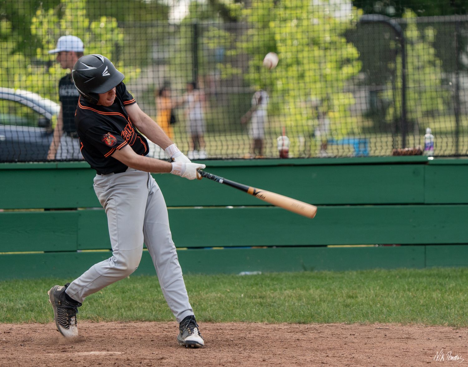 Baseball player in gray uniform swinging a wooden bat during a summer game on a dirt infield.