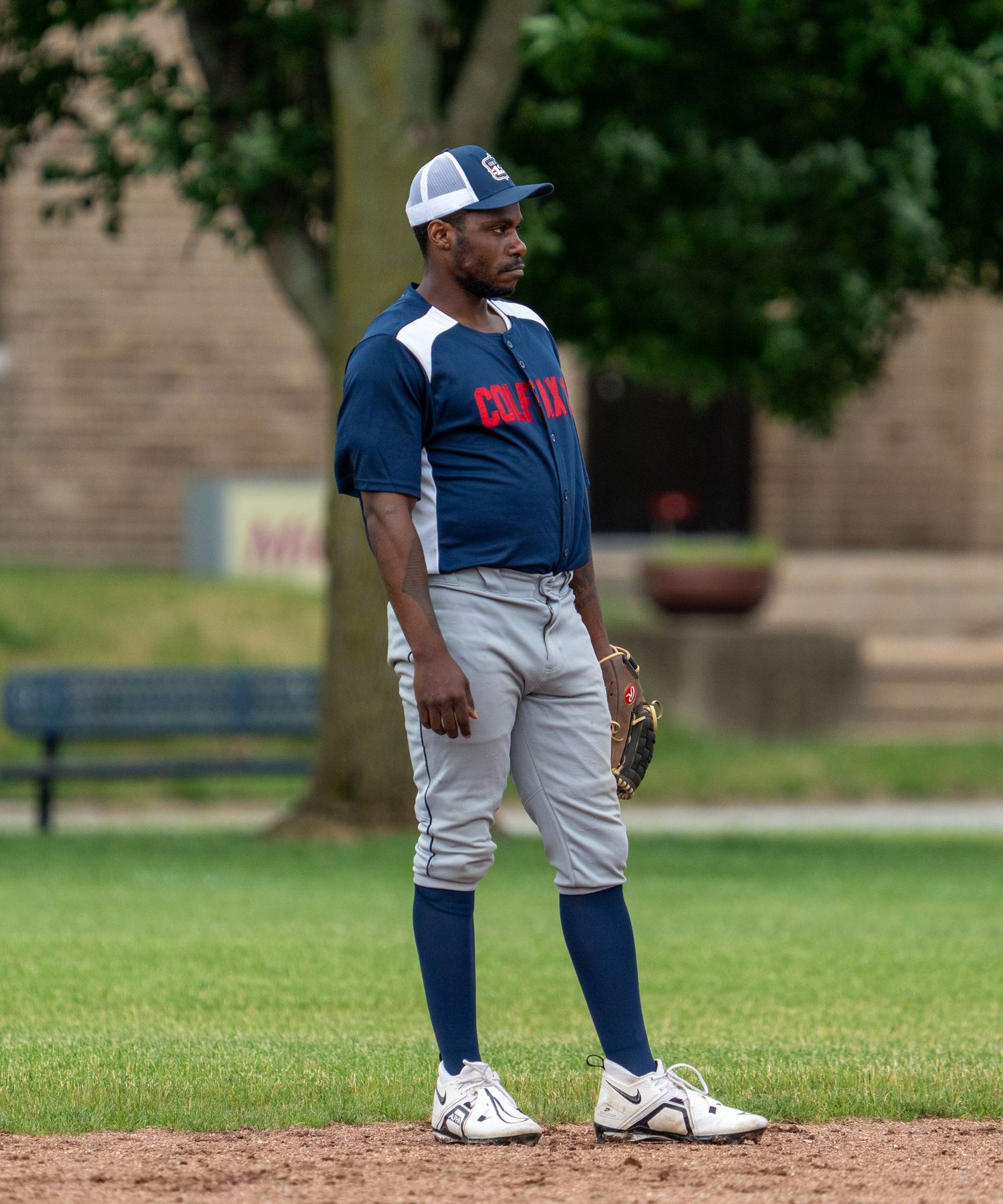 Adult baseball player in navy uniform and cap stands on field holding glove.