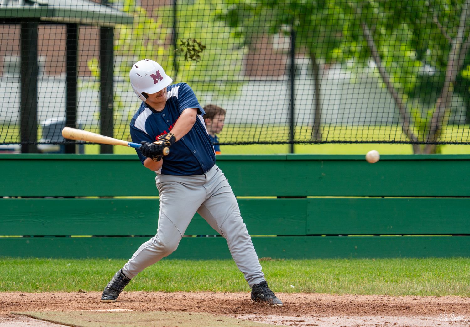 Youth baseball batter swings at a pitch during a game, wearing a white helmet and navy blue uniform.