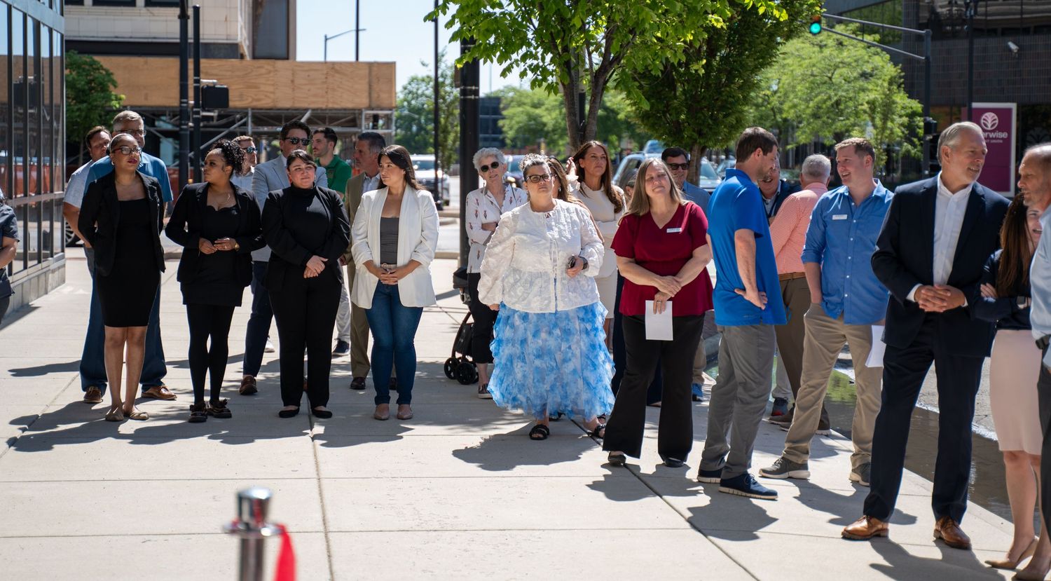 Diverse group of people standing on a sunny urban sidewalk during an outdoor community event or tour.